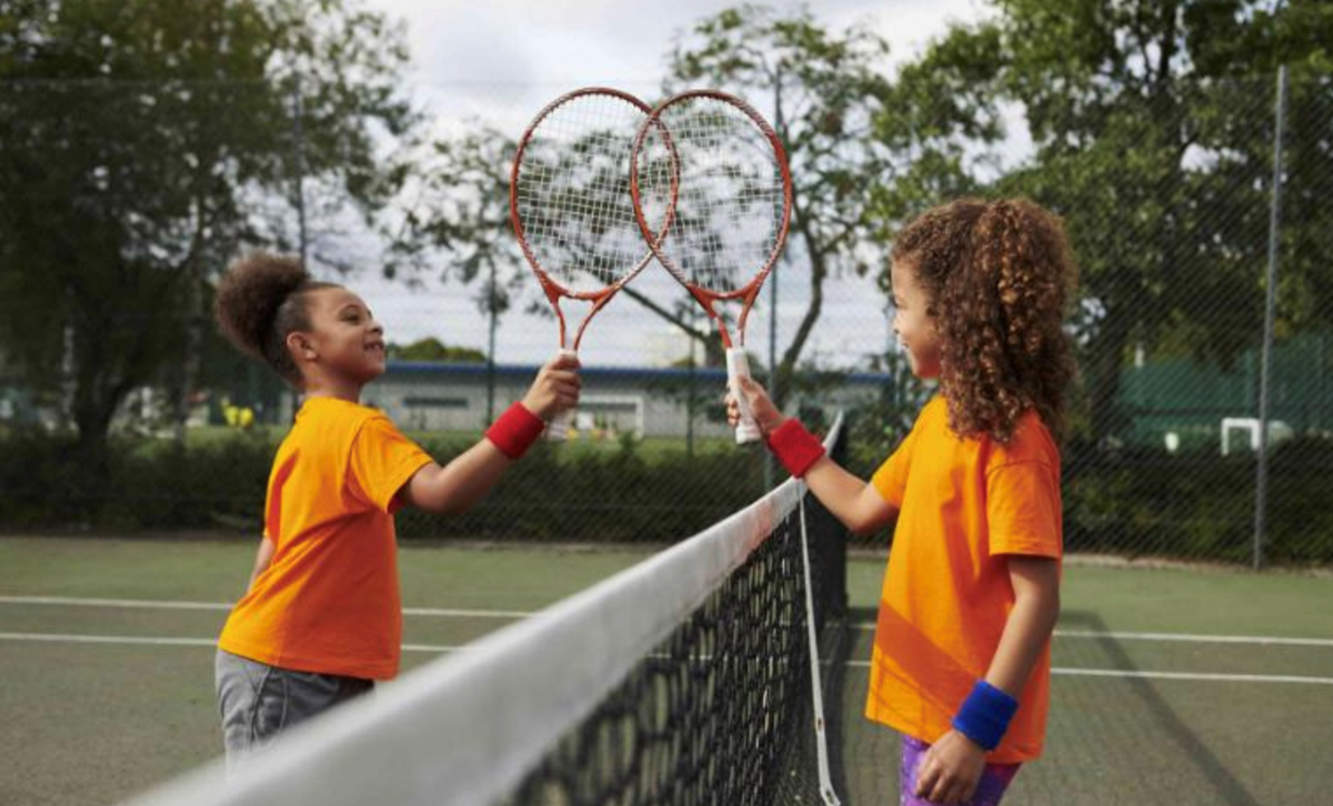 two little kids touching rackets by a tennis net