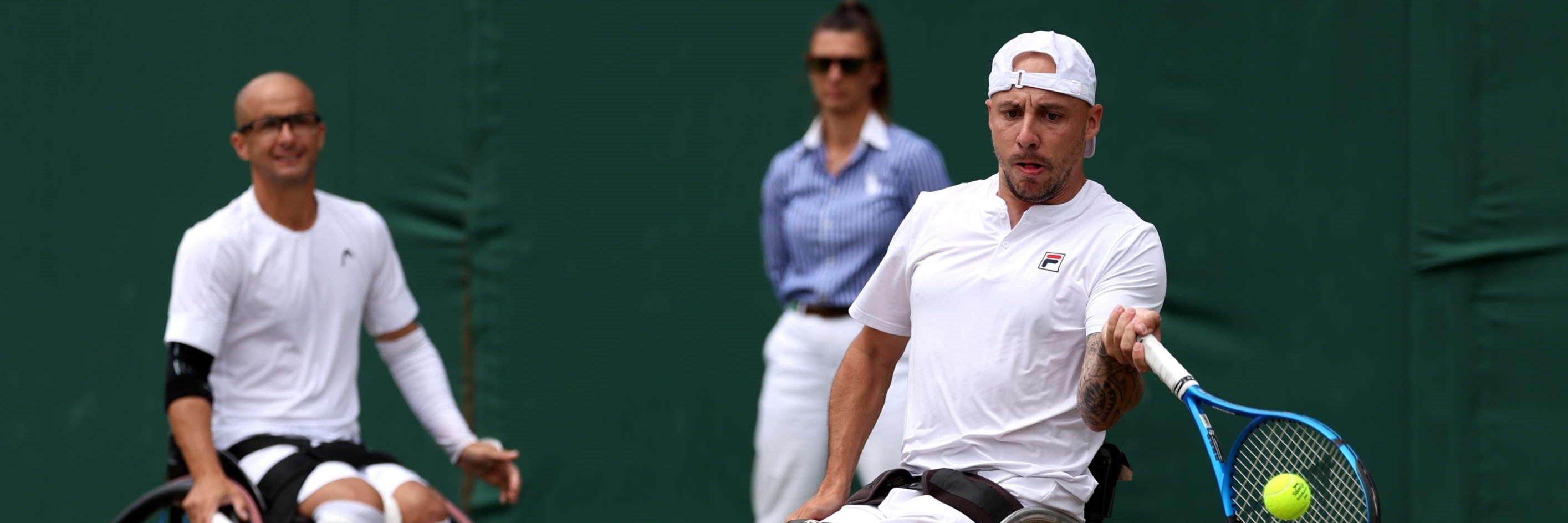 Andy Lapthorne preparing to hit a forehand on court while Guy Sasson is sat behind him