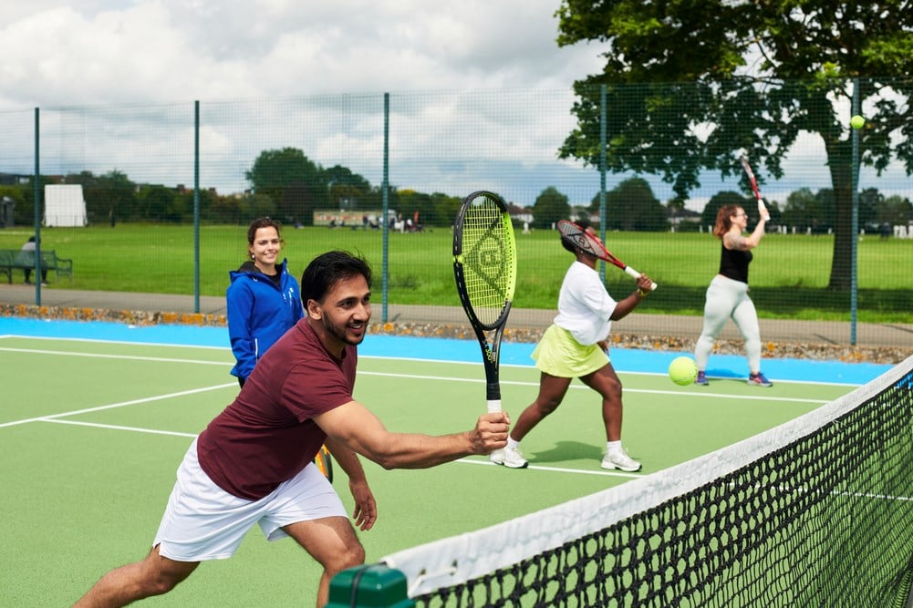 A first time tennis player practicing making a shot at the net alongside two other people.