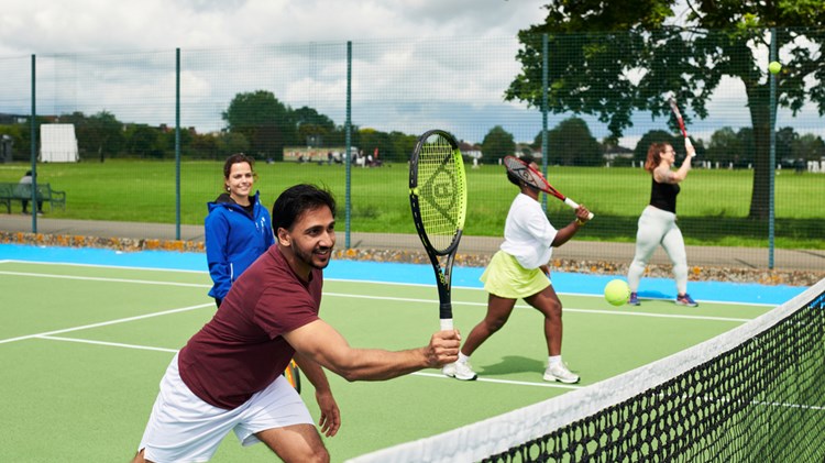 A first time tennis player practicing making a shot at the net alongside two other people.
