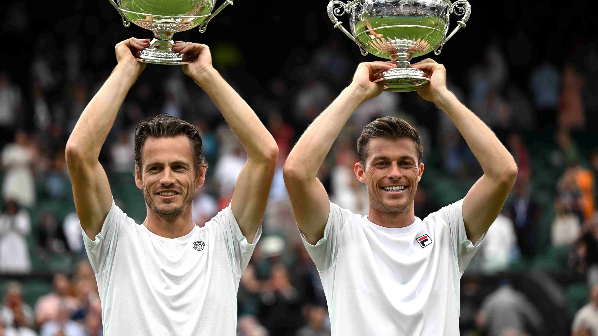 Neal Skupski and Wesley Koolhof lifting their championship trophies above their heads on court at Wimbledon