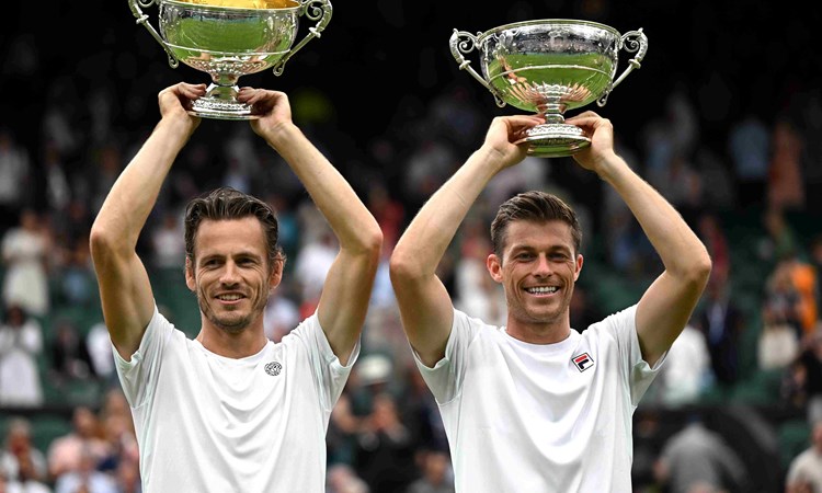 Neal Skupski and Wesley Koolhof lifting their championship trophies above their heads on court at Wimbledon