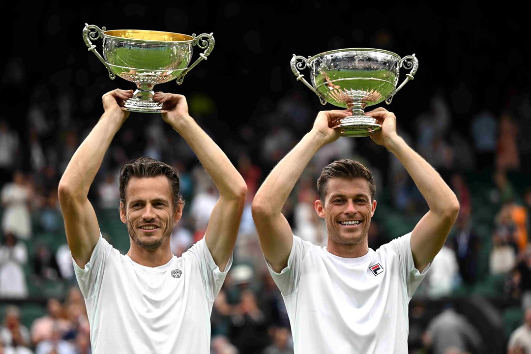 Neal Skupski and Wesley Koolhof lifting their championship trophies above their heads on court at Wimbledon