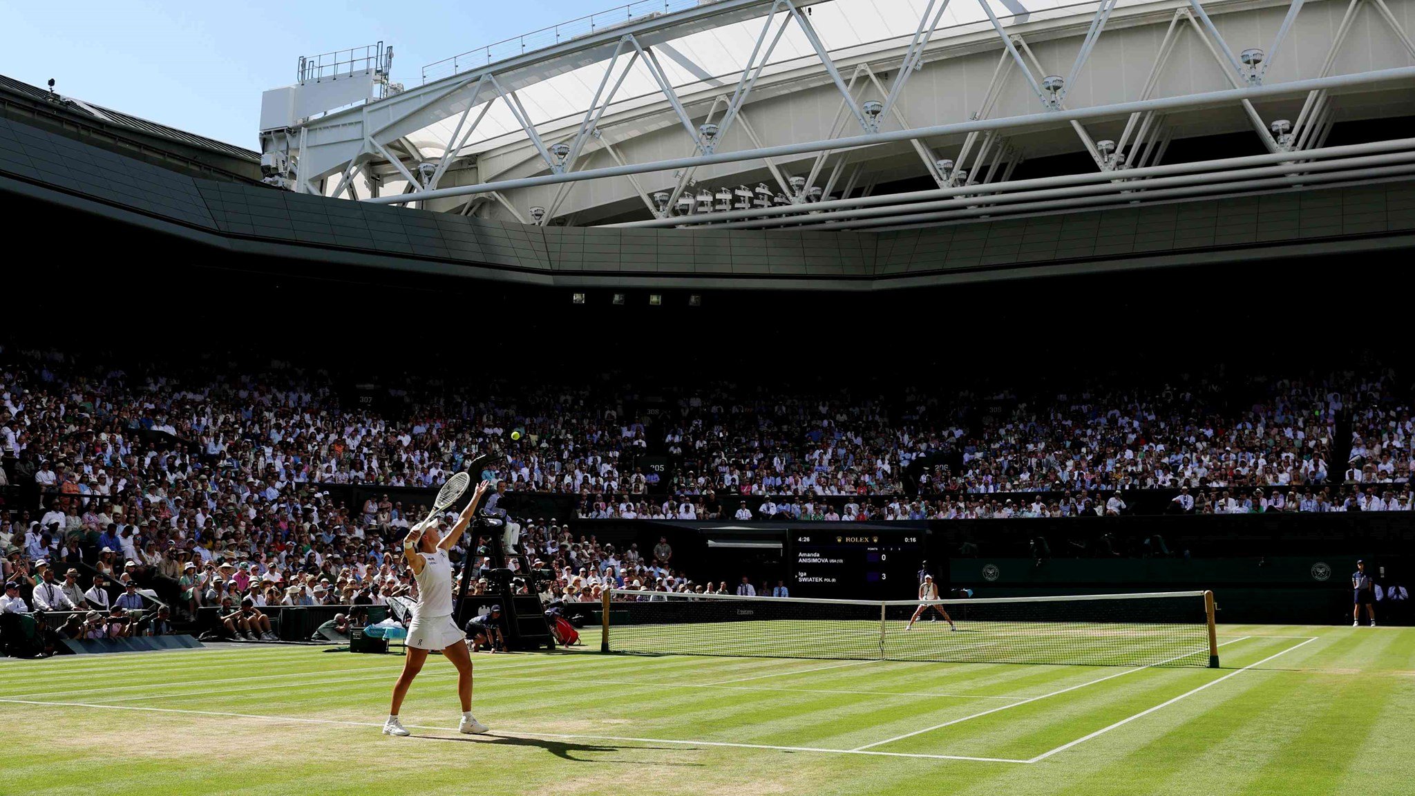 A view from the back corner of Wimbledon's centre court as a female player tosses the ball up to serve in front of a packed out crowd