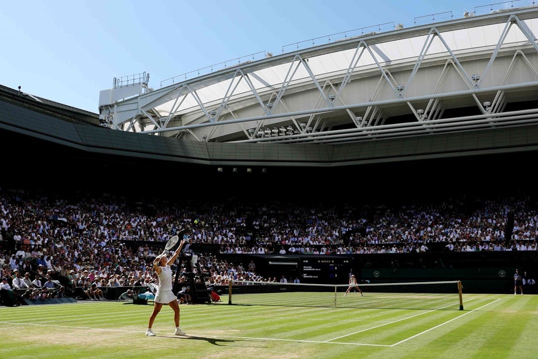 A view from the back corner of Wimbledon's centre court as a female player tosses the ball up to serve in front of a packed out crowd