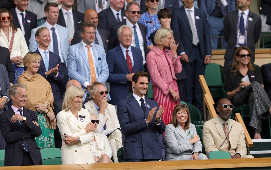 The Royal Box guests with Roger Federer at the front at Wimbledon standing up smiling and clapping while looking onto court