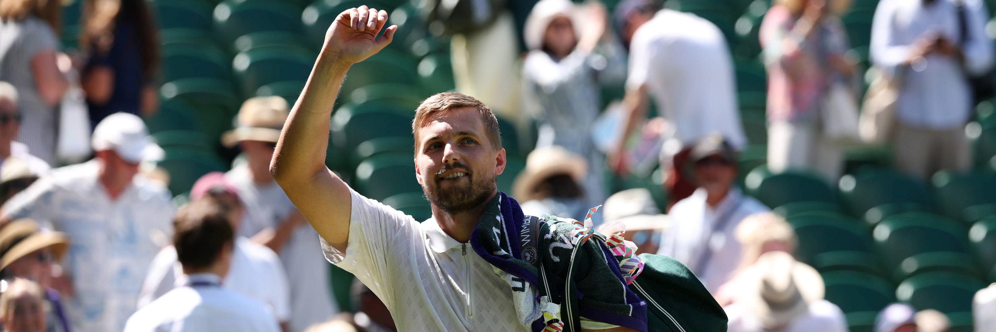 Lloyd Glasspool raising his hand to wave to the Wimbledon crowd, towel over his shoulder, holding onto his men's doubles trophy