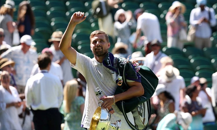 Lloyd Glasspool raising his hand to wave to the Wimbledon crowd, towel over his shoulder, holding onto his men's doubles trophy