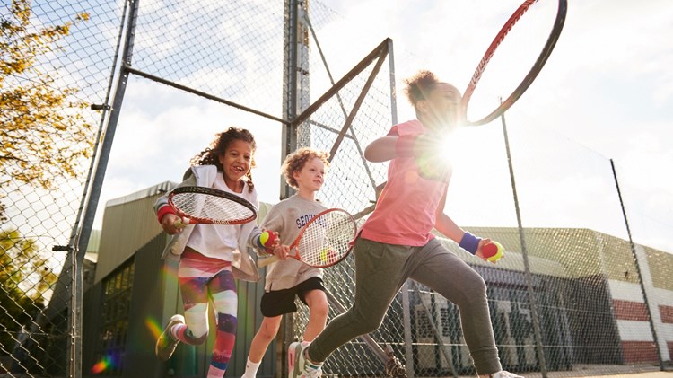 Kids running on to court with a ball and racquet in hand