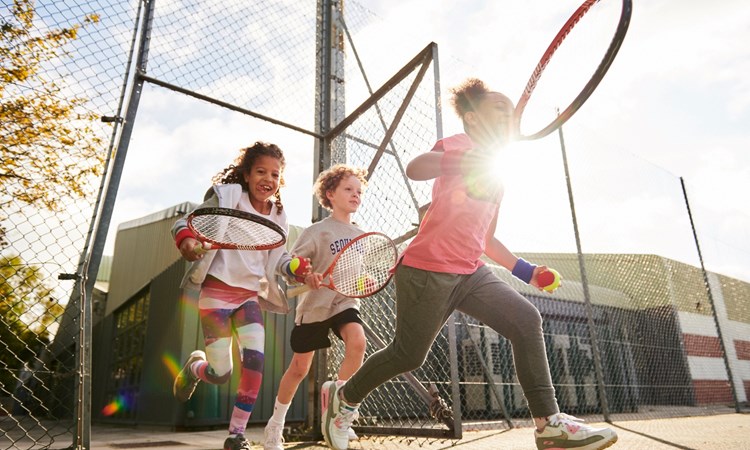 Kids running on to court with a ball and racquet in hand