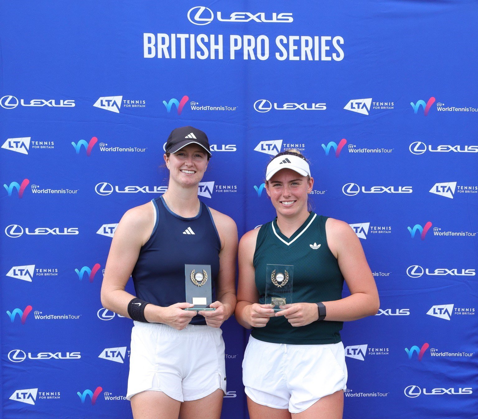 Two women stand in front of a blue background holding glass trophies. ABove them read the words, 'Lexus British Pro Series'