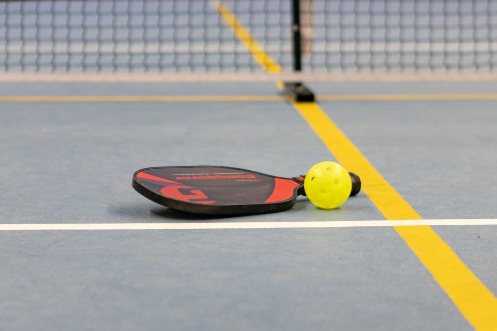 A pickleball paddle and ball lying on a court