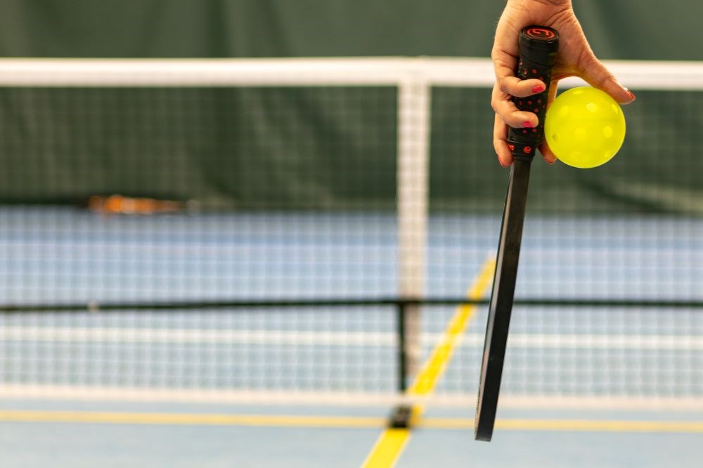 A hand holding a pickleball paddle and ball