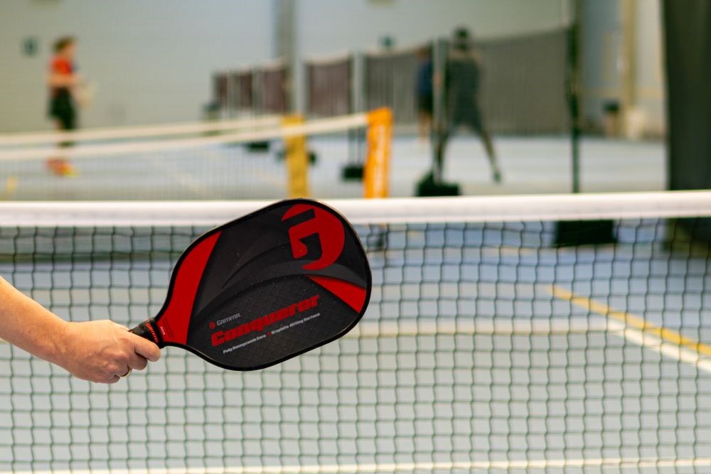 Someone holding a pickleball paddle at the net