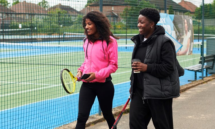 Two women walking to to the tennis court.