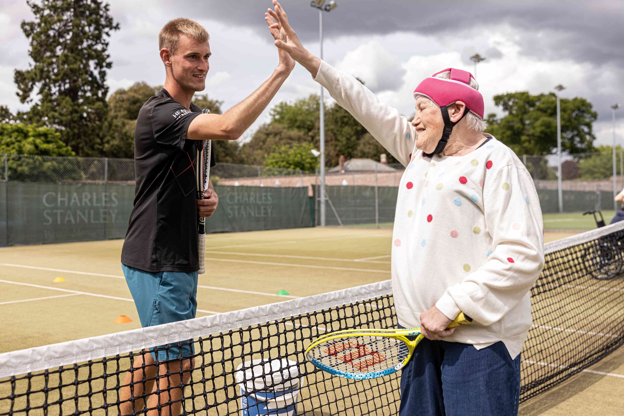 A sensory tennis participant high fiving the coach over the net.