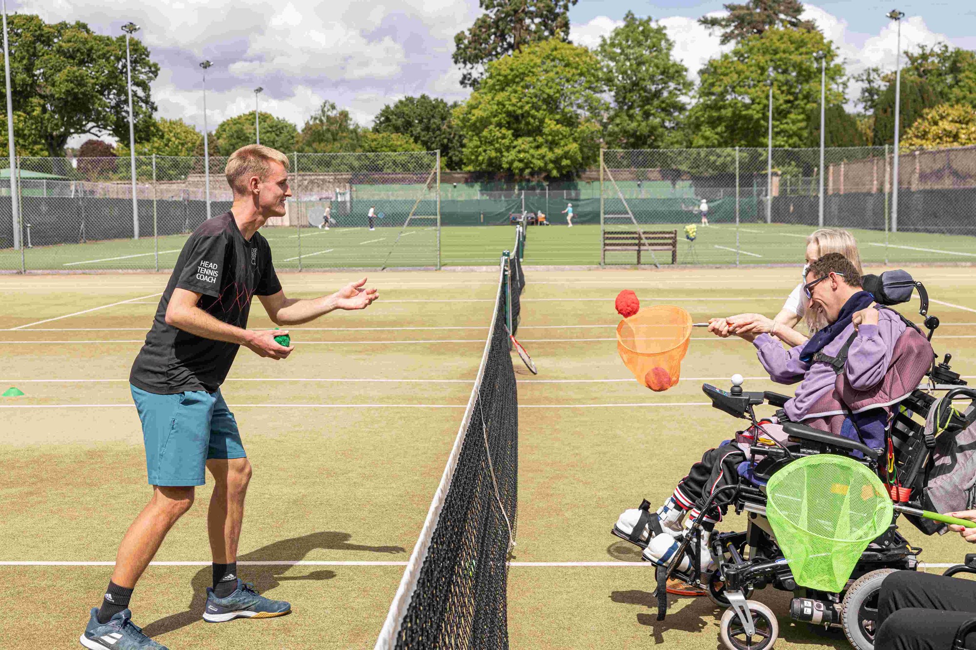A coach throwing soft balls to sensory tennis participants to catch in nets on sticks.