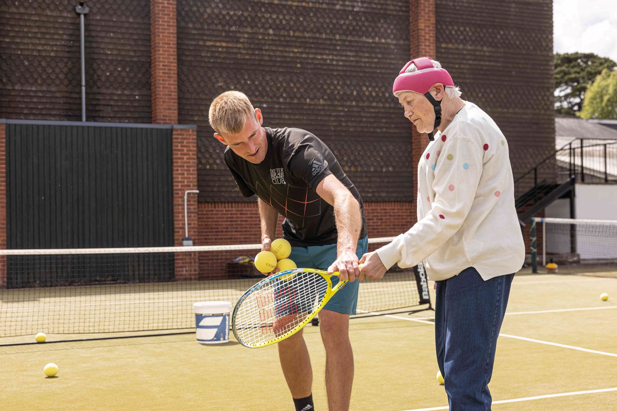 A tennis coach helping a sensory tennis participant to adjust their grip on the racket.