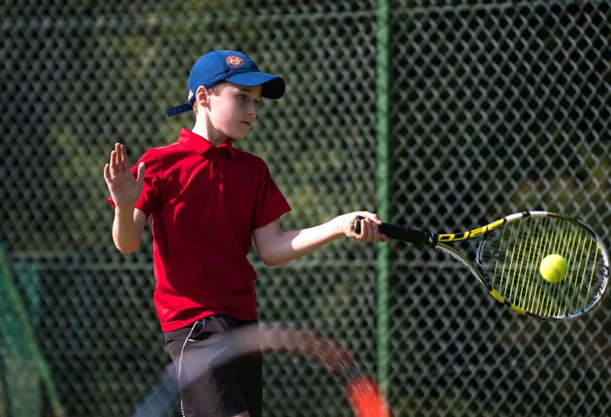 Young boy hits a forehand while playing tennis