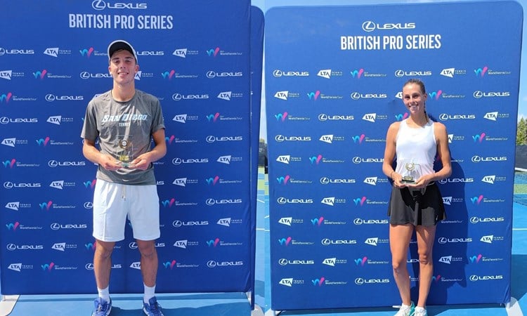 Two people, one man and one woman, stood holding glass trophies in front of a large blue board with small sponsor logos on it