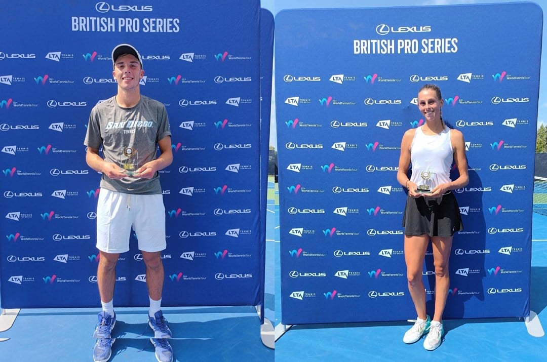 Two people, one man and one woman, stood holding glass trophies in front of a large blue board with small sponsor logos on it