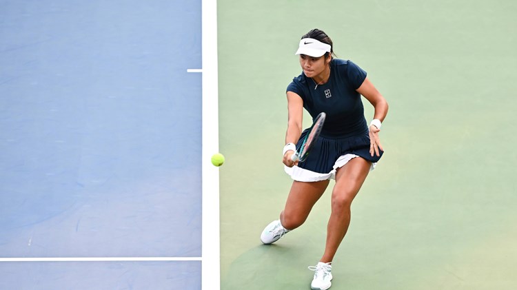Emma Raducanu hitting a backhand from behind the baseline on a hard court