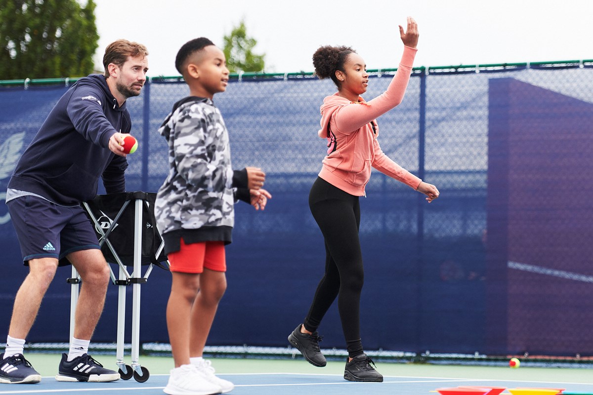 A tennis coach on court with two junior players