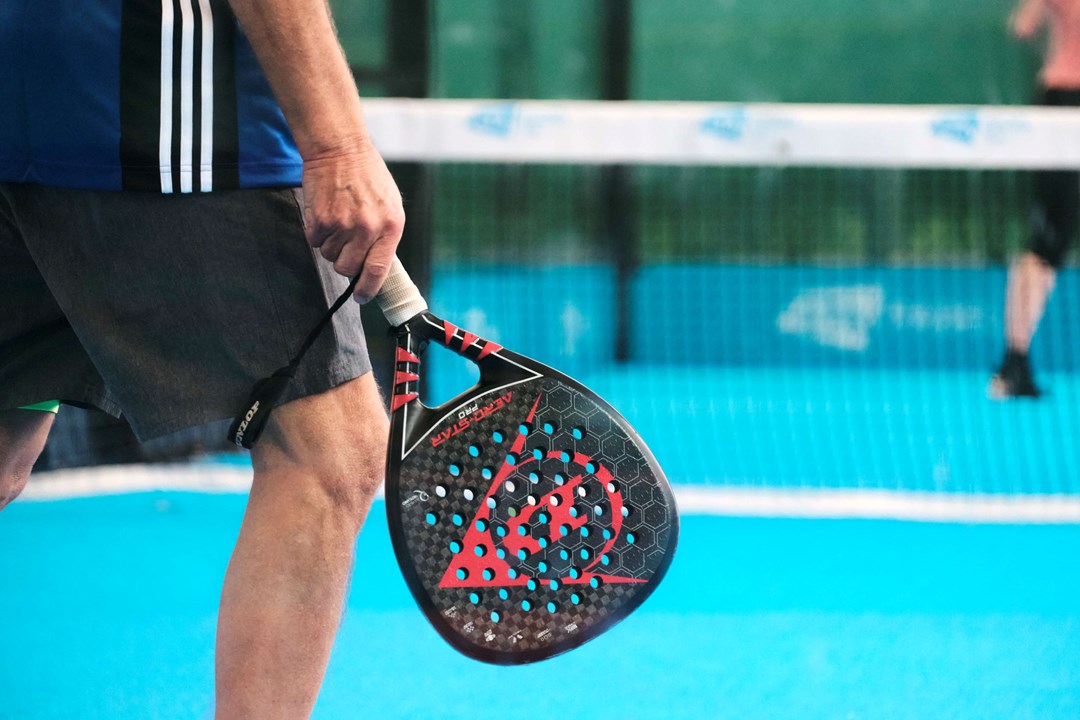 A padel bat being held by a man standing on a padel court