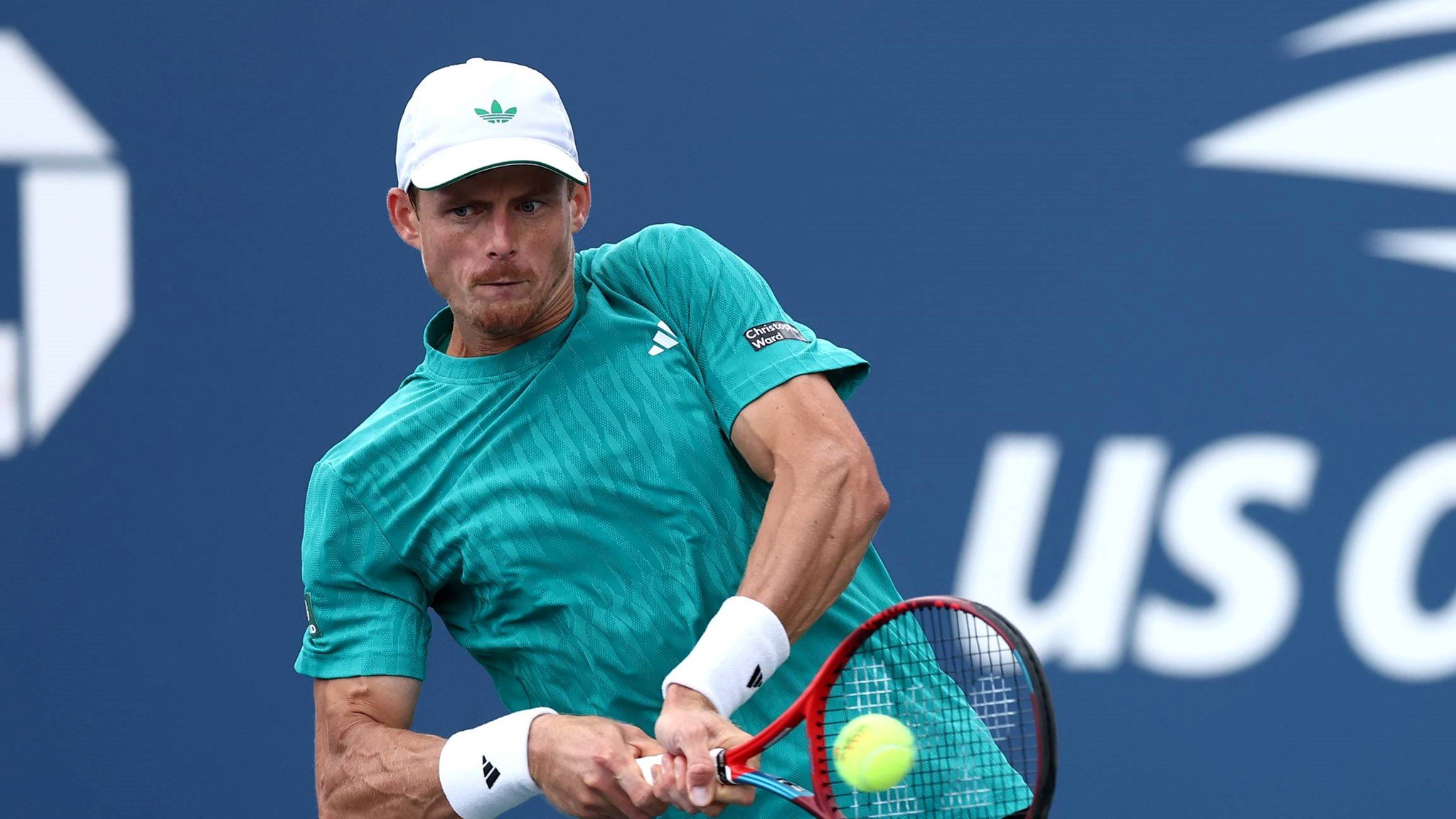 British tennis player Billy Harris wearing a teal Adidas top and hitting a backhand on court at the US Open
