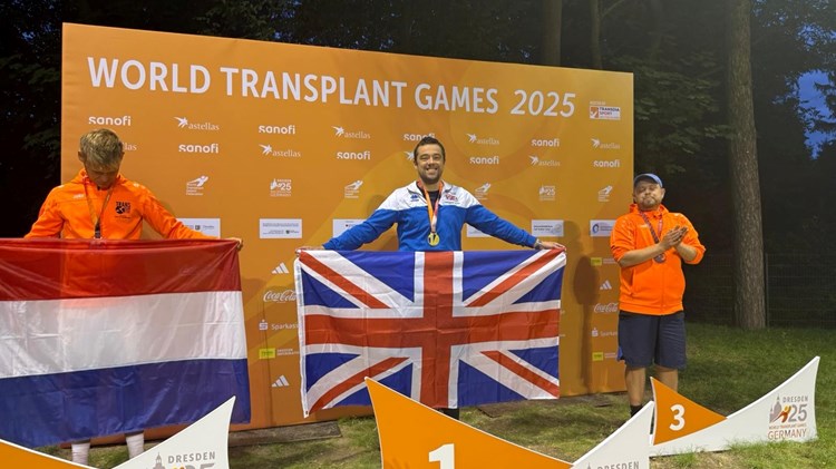 A man holding a British union flag stands in front of a large orange backdrop displaying the words 'World Transplant Games 2025'
