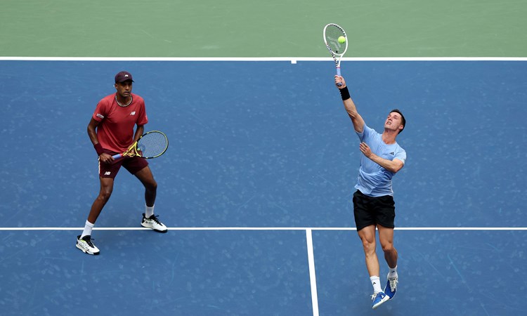 Joe Salisbury hitting an overhead smash while Rajeev Ram waits on court at the US Open