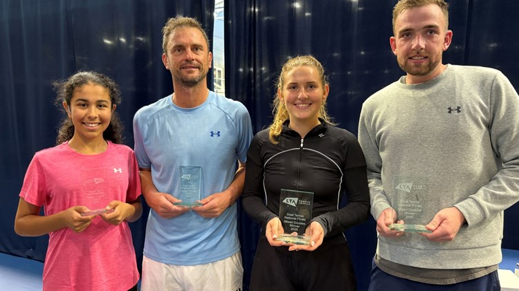 Four people, two men and two women (alternating woman, man, woman, man from left to right), stand holding glass trophies.