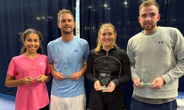 Four people, two men and two women (alternating woman, man, woman, man from left to right), stand holding glass trophies.