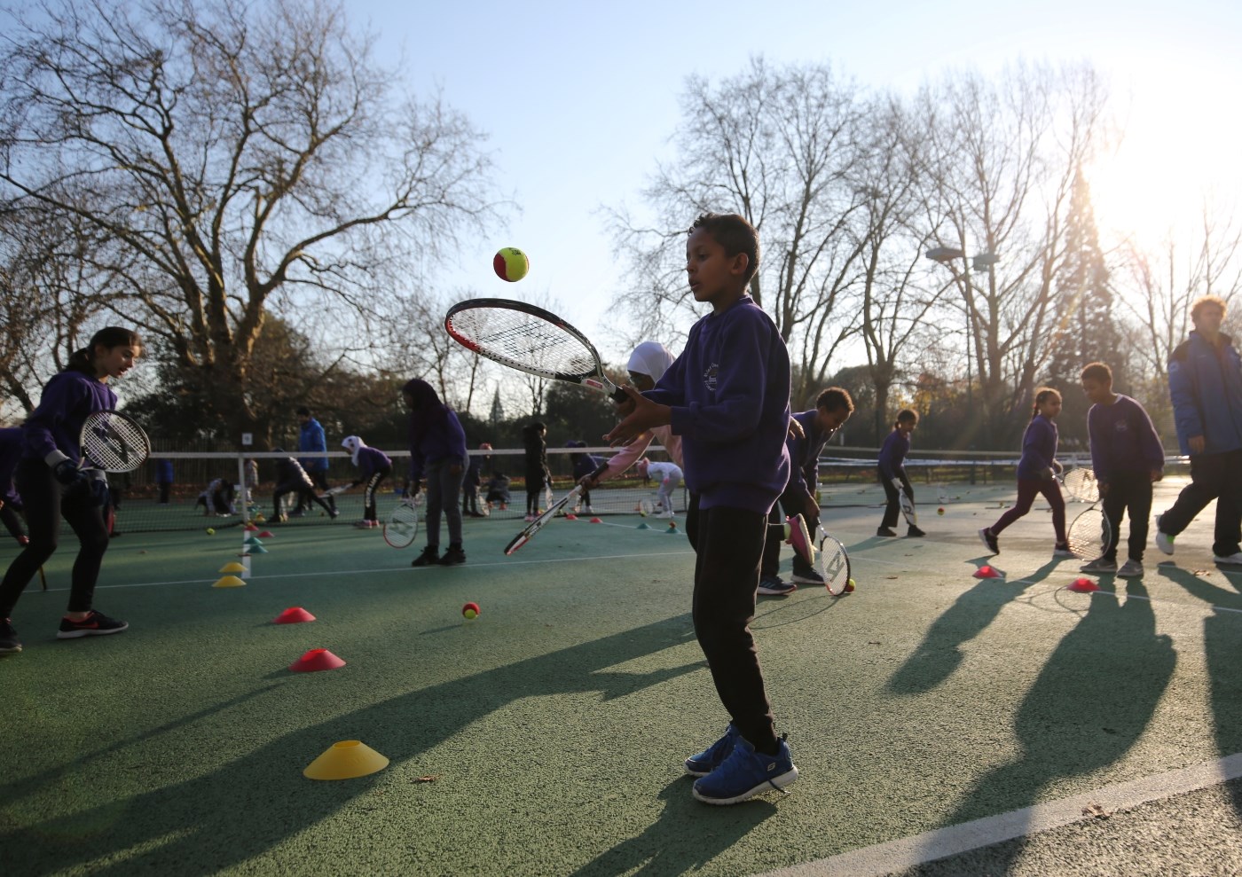 School children hitting tennis balls with rackets