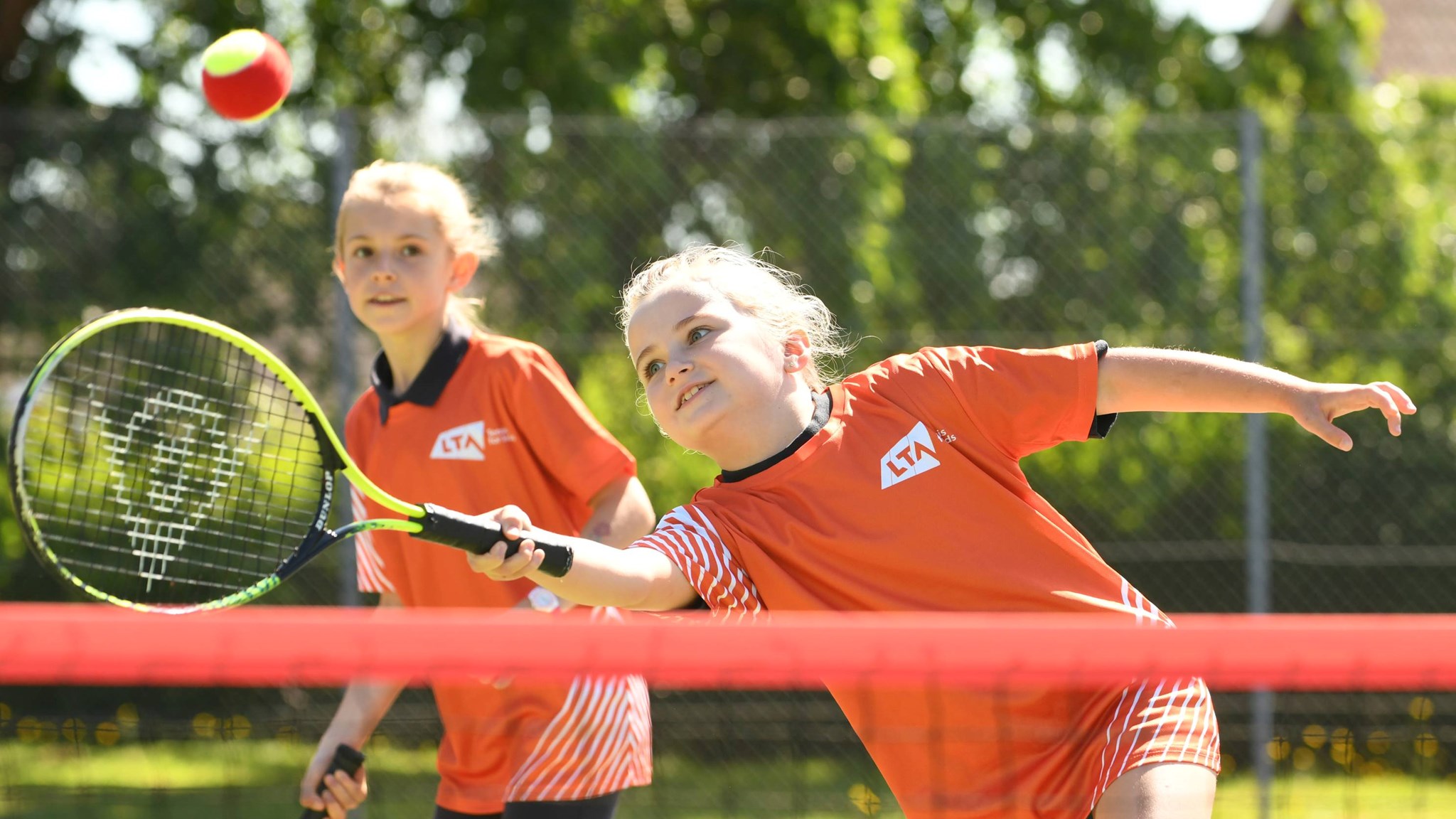 Young girl hitting a tennis ball over a net