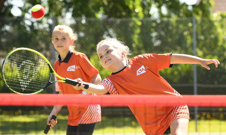 Young girl hitting a tennis ball over a net