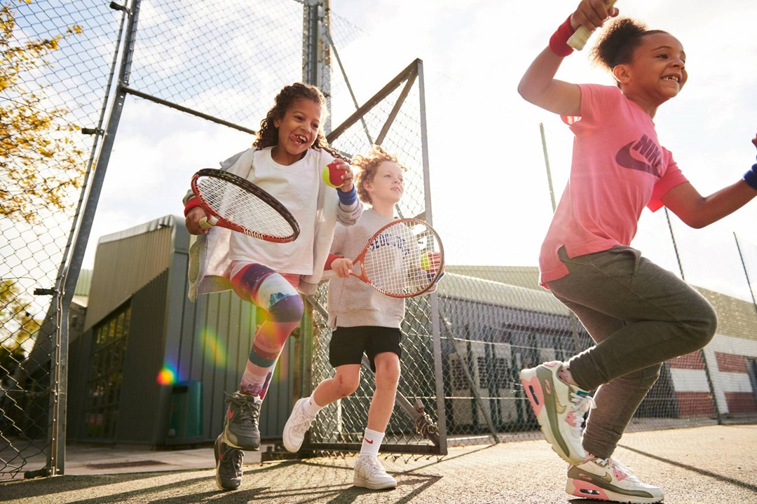 A group of kids running onto a tennis court