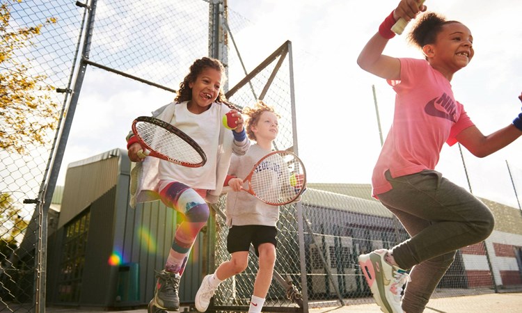 A group of kids running onto a tennis court