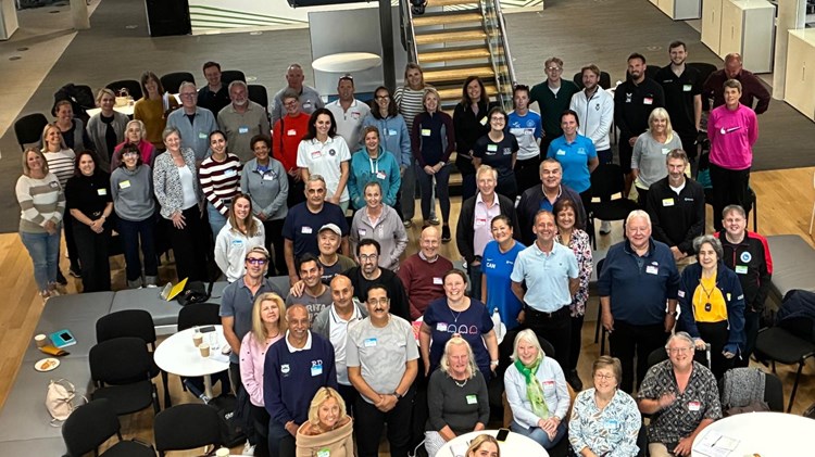 A large group of people stand smiling looking up at the camera