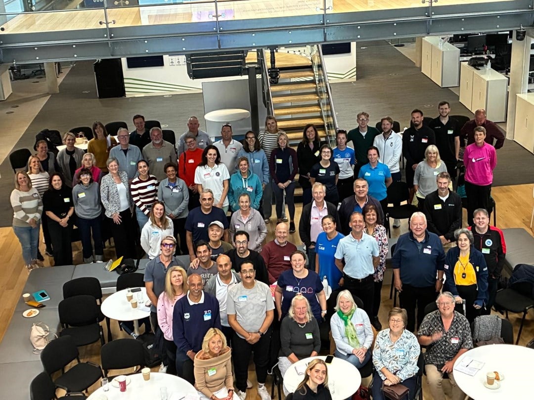 A large group of people stand smiling looking up at the camera