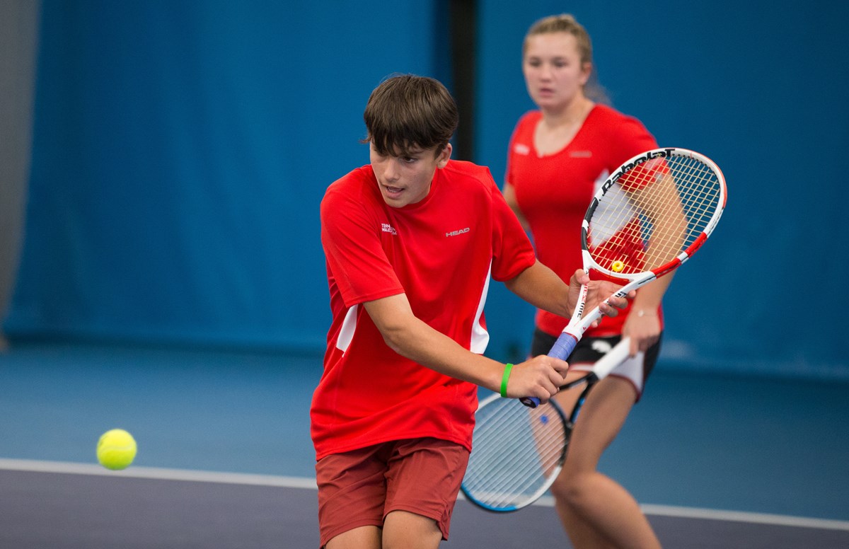 Young Welsh tennis player preparing to slice a backhand on an indoor tennis court