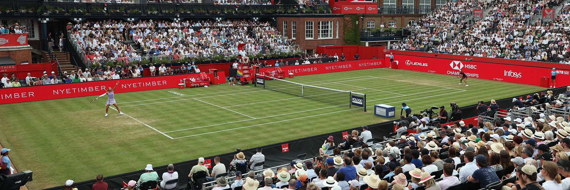 A view from the stands at the HSBC Championships  towards the Queen's Clubhouse while a player is serving on the grass court.