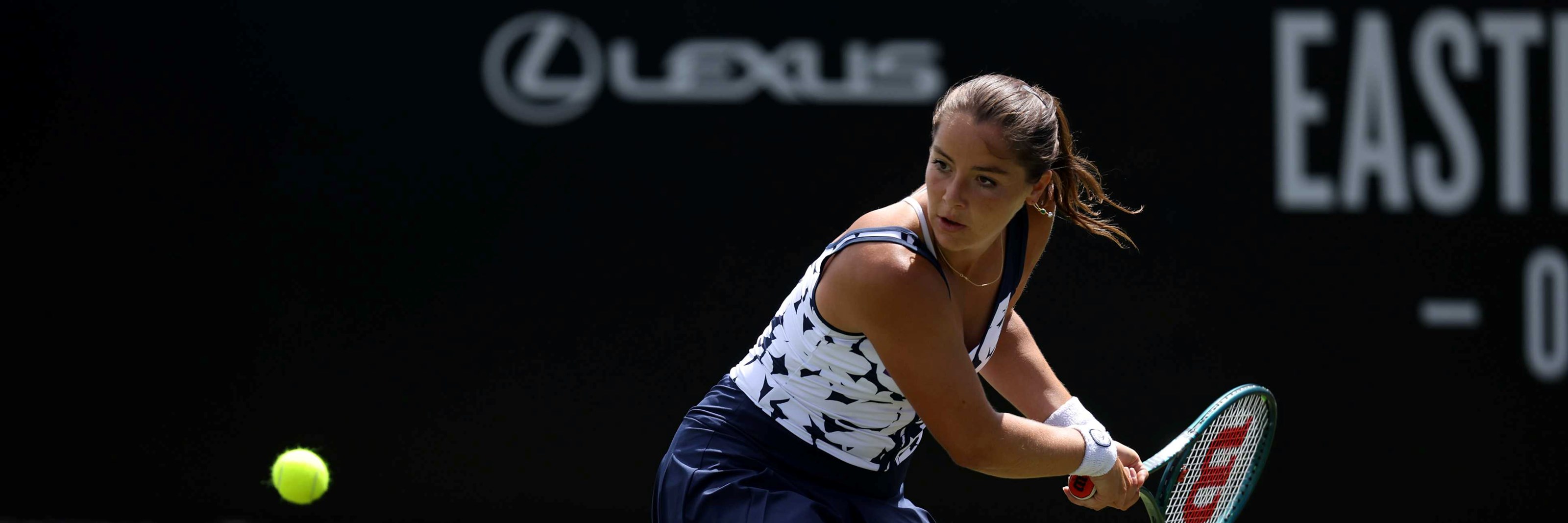Jodie Burrage bending down low on a grass court in preparation of hitting a backhand