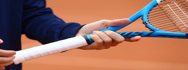 A person holding a blue tennis on a clay tennis court racket