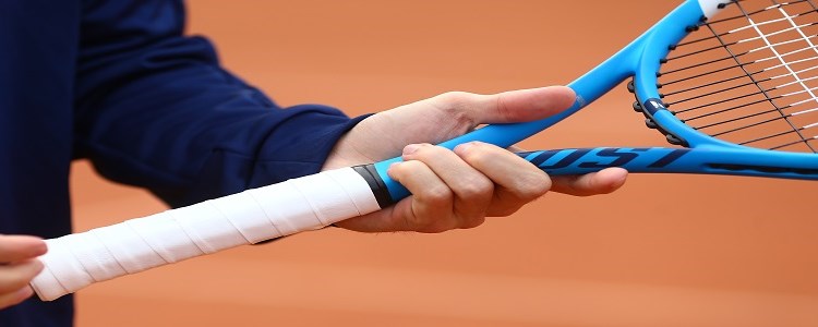 A person holding a blue tennis on a clay tennis court racket