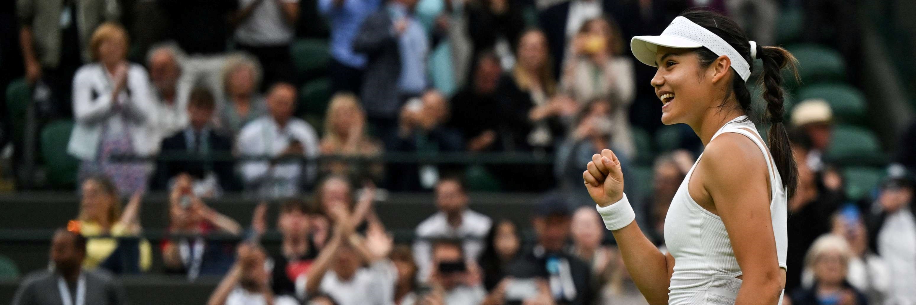 British tennis player Emma Raducanu smiling while tennis fans watch her on Centre Court at Wimbledon