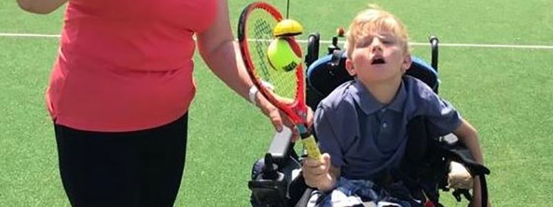 Young disabled boy playing tennis with a tennis coach