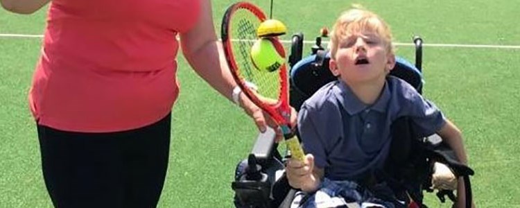 Young disabled boy playing tennis with a tennis coach