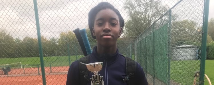 Annis Frimpong holding an award in front of a tennis court