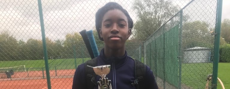 Annis Frimpong holding an award in front of a tennis court